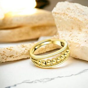 Gold adjustable ring on a marble counter top with sandstone in background