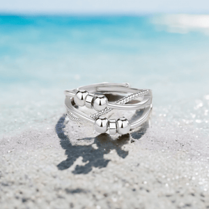 Silver triple band cross over anxiety ring with sliding beads on a beach