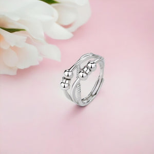 Silver triple band cross over worry ring on a pink surface