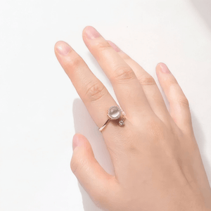 Woman's hand wearing a fidget spinner ring with an opal top on a white surface