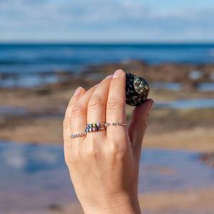 Woman's hand holding a shell wearing 3 anxiety rings in Australia sea background