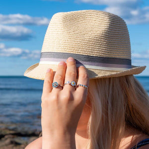 Woman touching straw hat with hand wearing three adjustable sterling silver rings on the beach