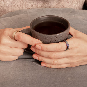 Woman holding a tea mug with both hands wearing spinner rings in gold and rainbow
