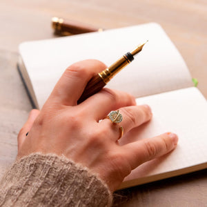 Woman wearing a planet anxiety ring that spins in gold holding a pen