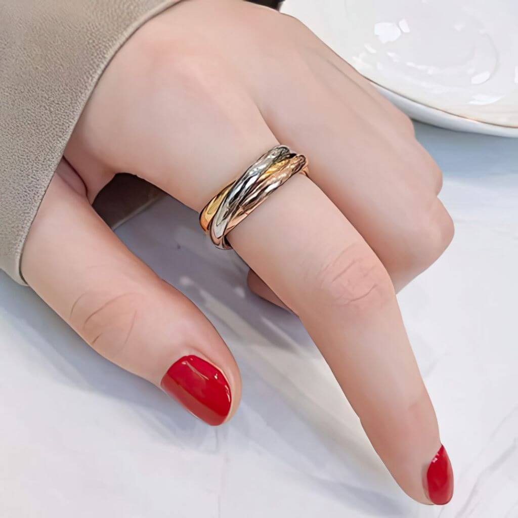 Hand wearing a gold ring with red nail polish on a neutral background