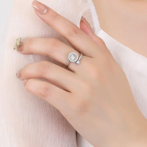 Close-up of a hand wearing a silver ring with a pearl-like center on a light background