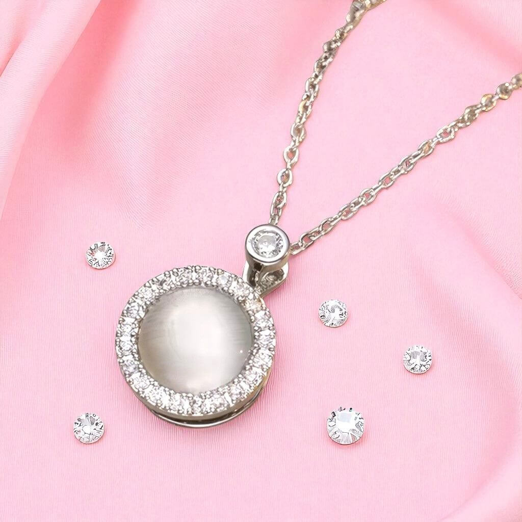 Silver necklace with a round pendant and matching earrings on a pink fabric background