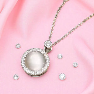 Silver necklace with a round pendant and matching earrings on a pink fabric background