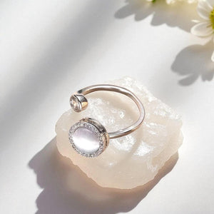 Silver ring with a gemstone on a light stone surface with flowers in the background