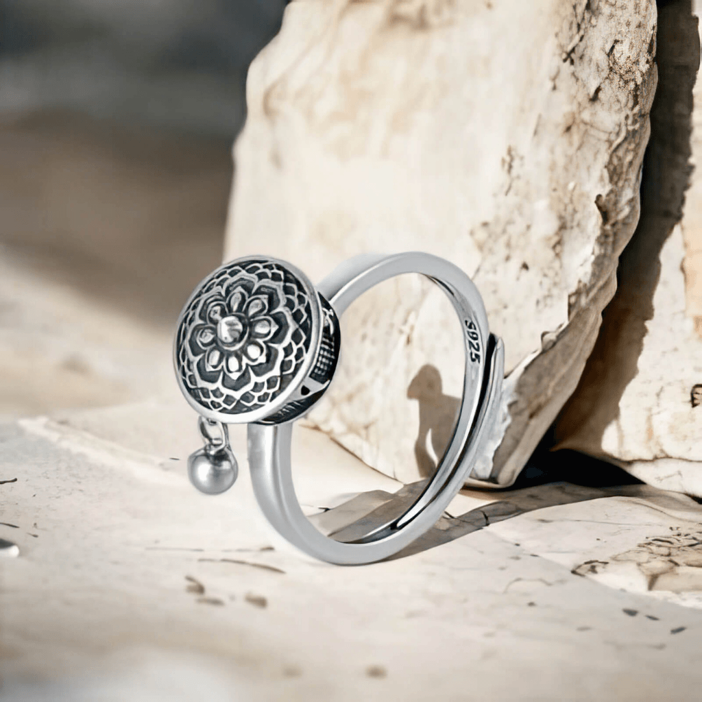 Silver ring with floral design and dangling bead on a stone background