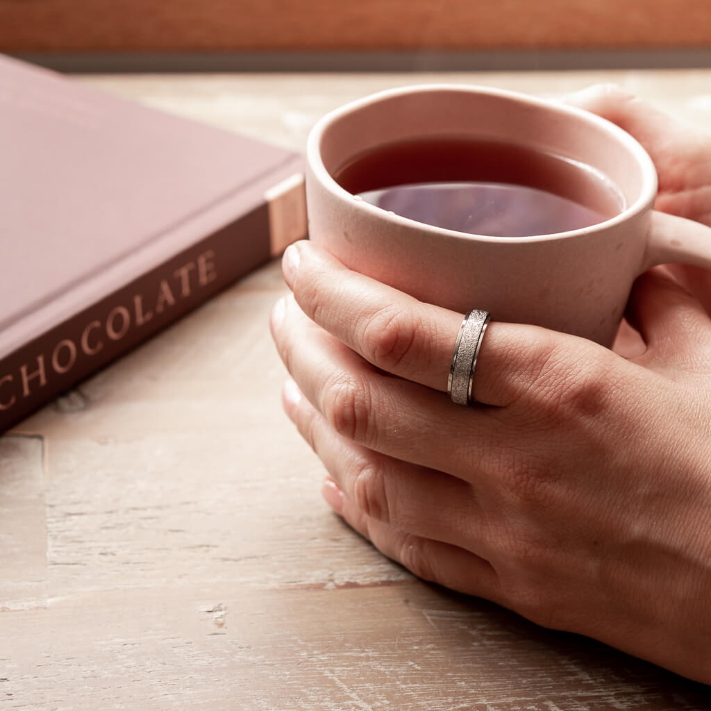 Woman's hand wearing silver spinning ring holding a cup of tea 