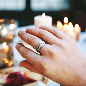 Woman's hand wearing a fidget ring with multi colored cubic zirconia on a background with lit candles