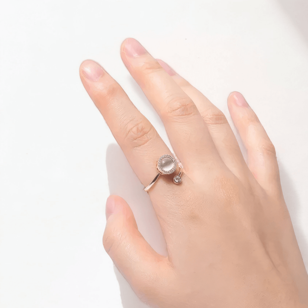 Woman's hand wearing a fidget spinner ring with an opal top on a white surface