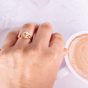 Woman's hand wearing a gold fidget ring next to a coffee mug on a grey surface