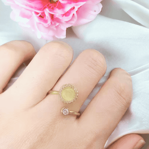 Woman's hand wearing a gold fidget ring with an opal top next to a peony