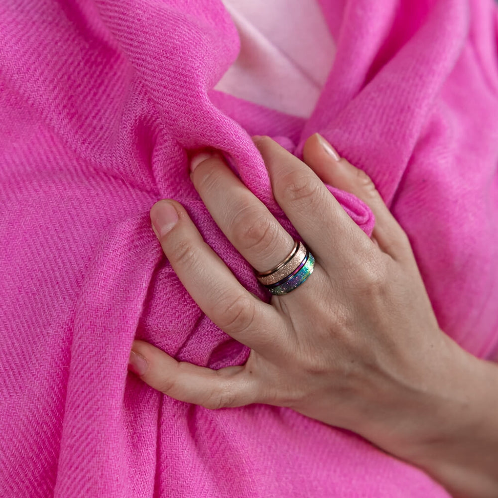 Woman's hand wearing gold and rainbow spinning rings Australia holding a pink shawl 