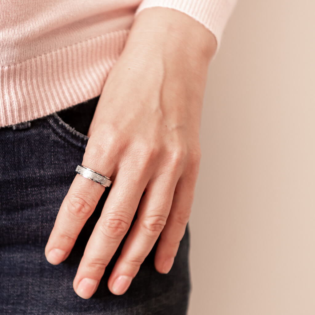 Woman's hand wearing a silver spinning ring for anxiety on black jeans