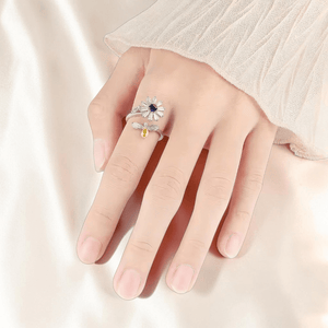 Hand wearing rhodium plated 925 silver daisy spinner fidget ring on cream silk background
