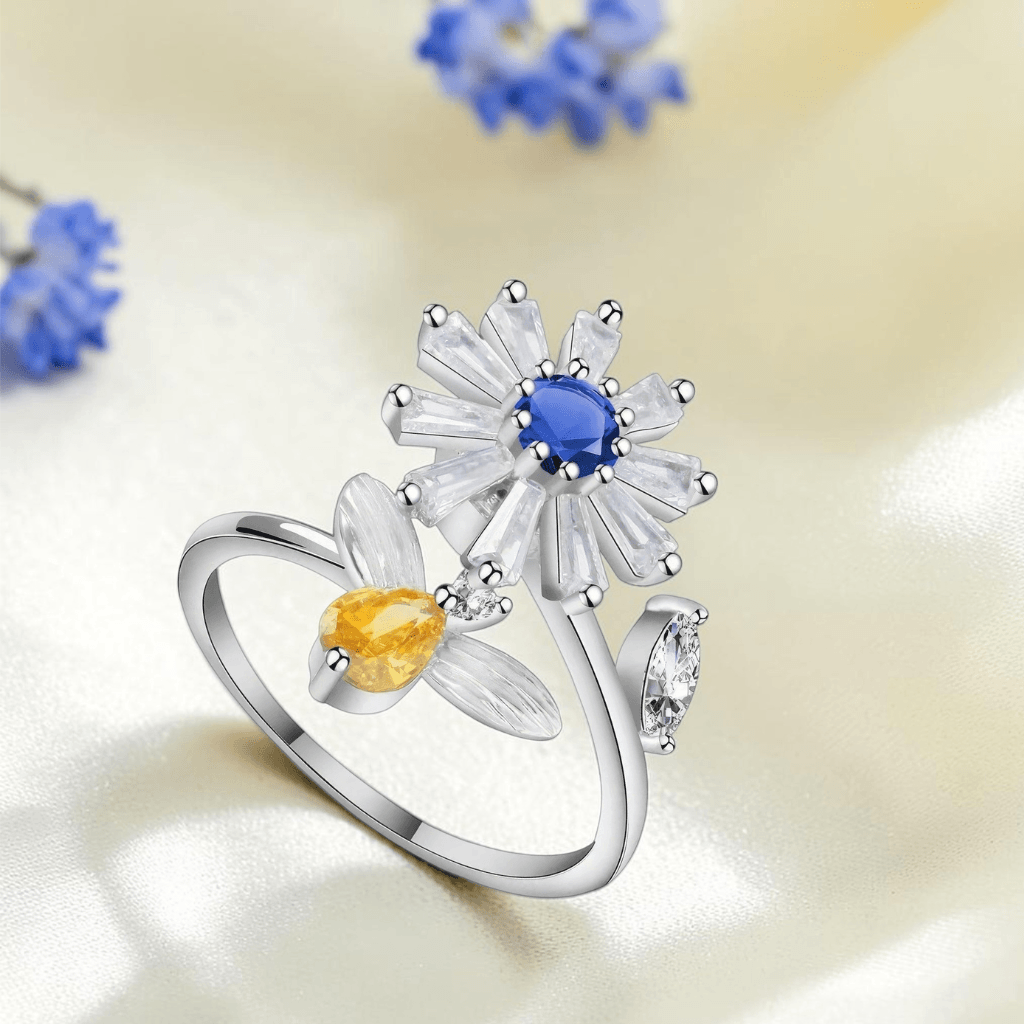 Silver daisy spinner fidget ring with blue centre stone and amber flower bud styled with blue dried flowers on cream silk