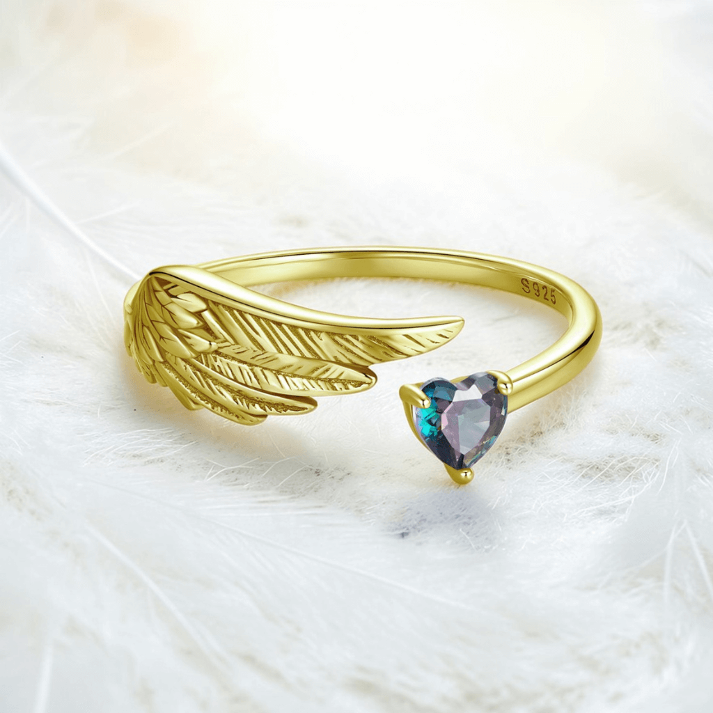 Gold angel wing heart ring with S925 stamp and heart shaped gemstone on feather background