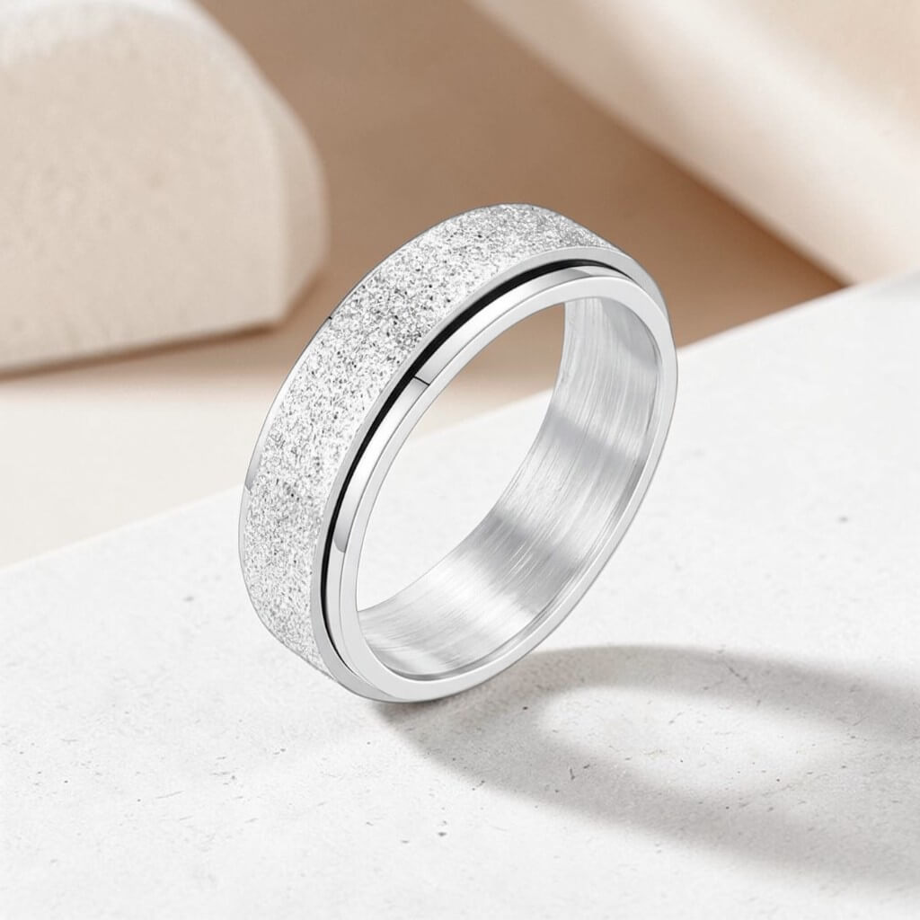 sterling silver spinner anxiety ring with textured band and soft shadow on neutral stone surface