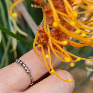 Finger wearing a silver beaded adjustable ring next to a yellow flower