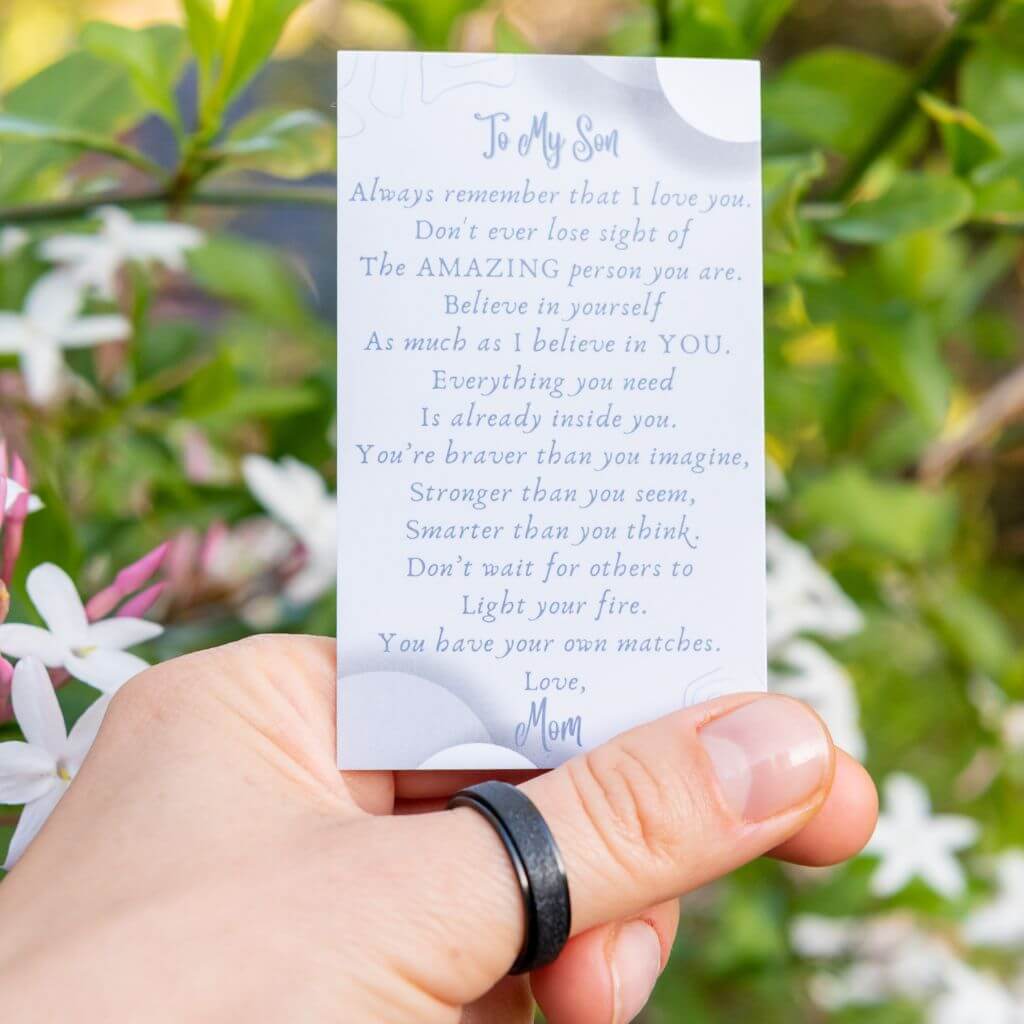 Woman's hand wearing a black spinning ring holding a message card for son