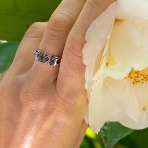 Woman's hand wearing a calming ring with flowers next to a yellow flower