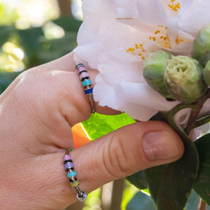 Woman's hand wearing colorful rings with beads next to a white flower