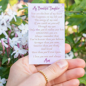 Woman's hand wearing a gold beaded adjustable ring holding a message card for daughter