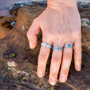 Woman's hand on a rock wearing 3 stainless steel band fidget rings