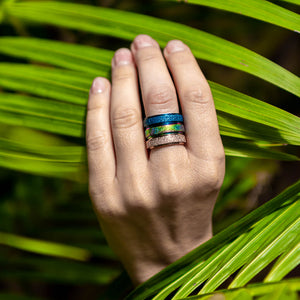 Woman's hand wearing blue rainbow gold spinning rings holding a palm leaf