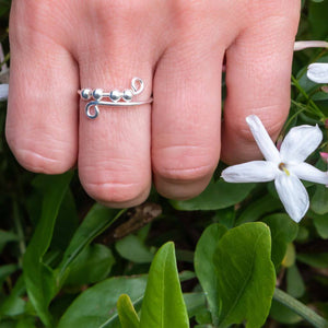 Woman's hand wearing a sterling silver ring with beads next to white flowers