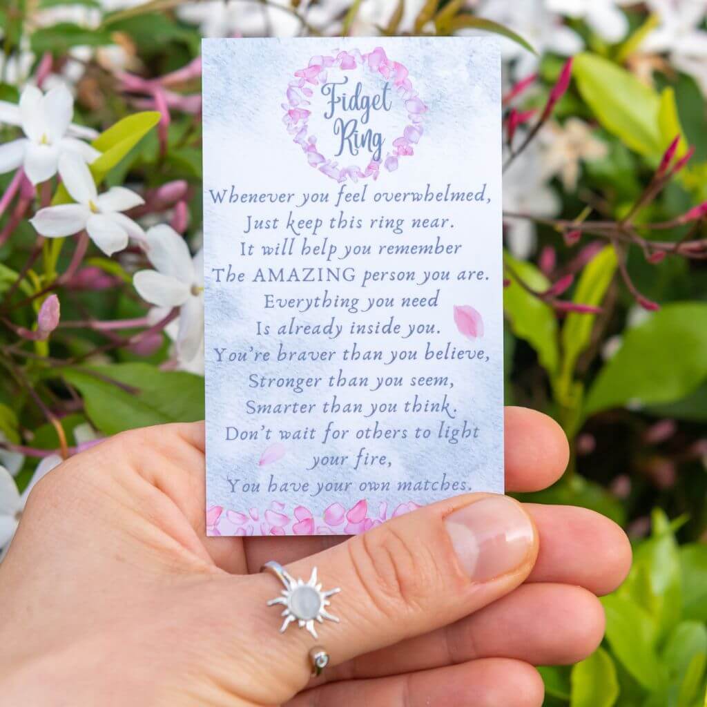 Woman's hand wearing a sun spinner fidget ring holding a message card for friend