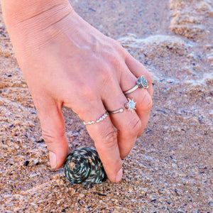 Woman's hand wearing 3 stress rings holding a shell on sand background