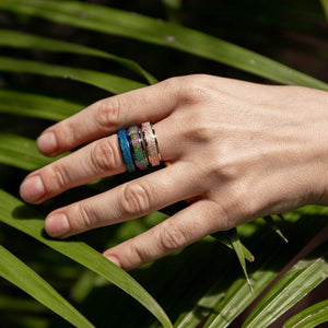 Woman's hand wearing tree spinner rings rainbow, gold, blue on green background