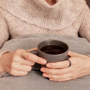 Woman wearing two spinner rings in rainbow and gold holding a mug with both hands